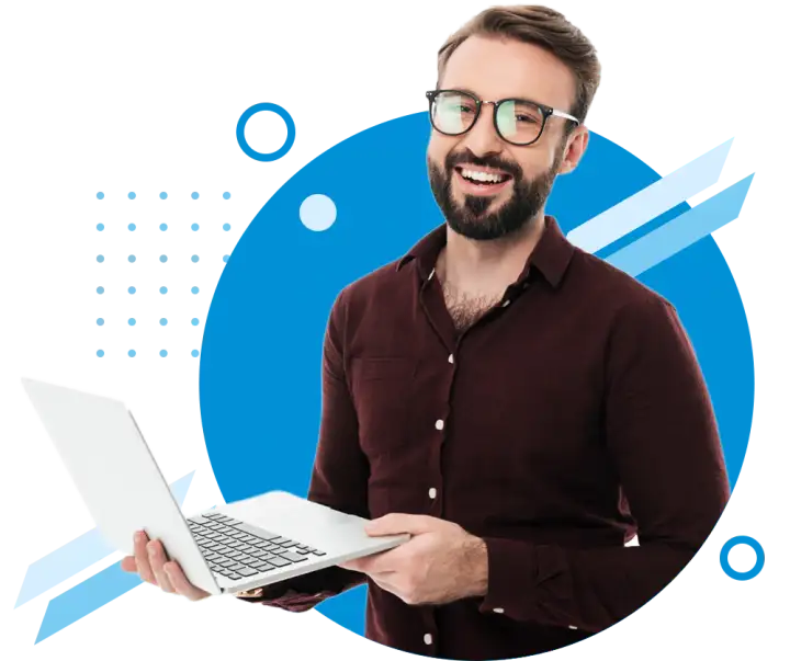 A well groomed man with a beard and glasses holds a laptop in his hands, he expresses happiness